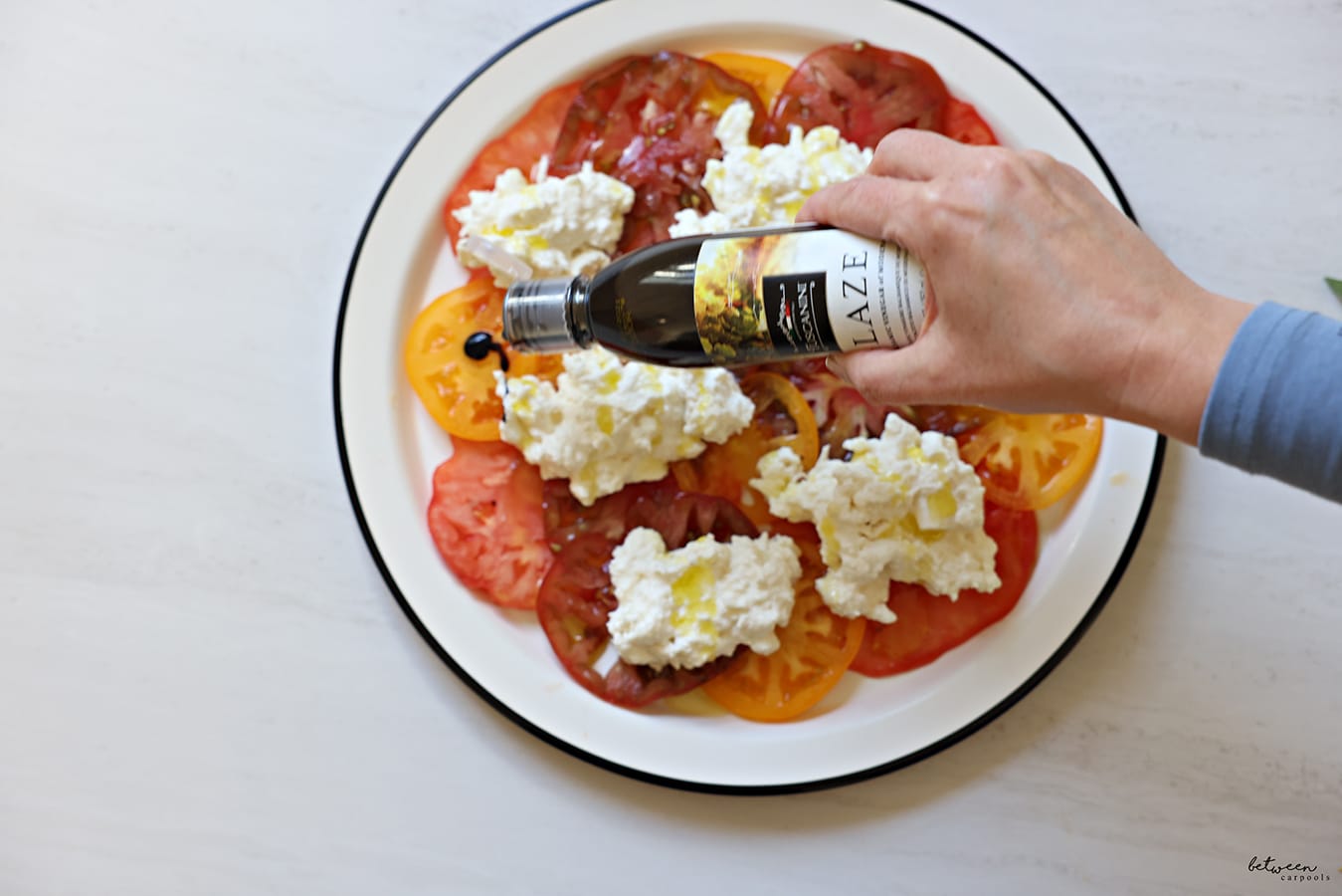 olive oil and balsamic glaze over dollops of soft cheese on tomatoes - carpaccio style - on a round plate