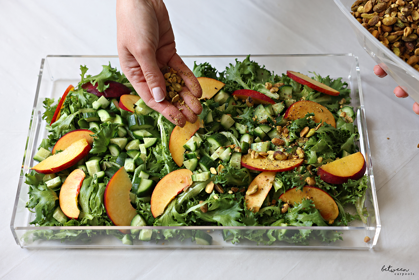 added cucumbers, nectarines, nuts to salad greens on a lucite platter.