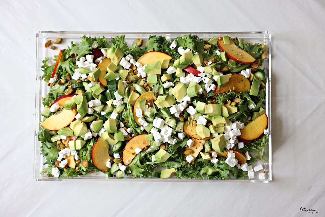 Avocado and feta added to salad greens + cucumbers, nectarines, and nuts on a lucite platter.
