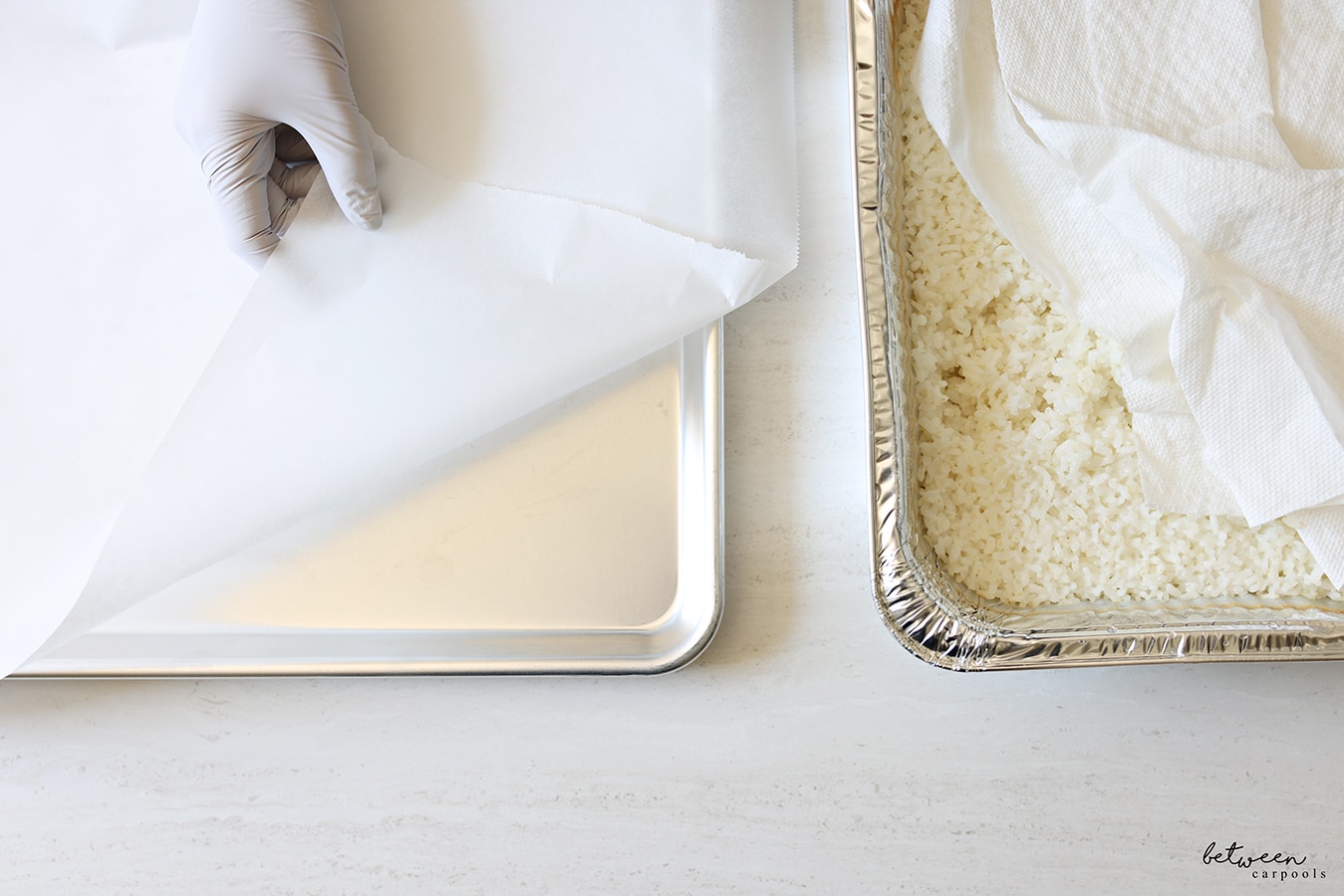Prepared sushi rice in a 9x13 foil pan. Placing parchment paper onto a metal baking sheet with a gloved hand.