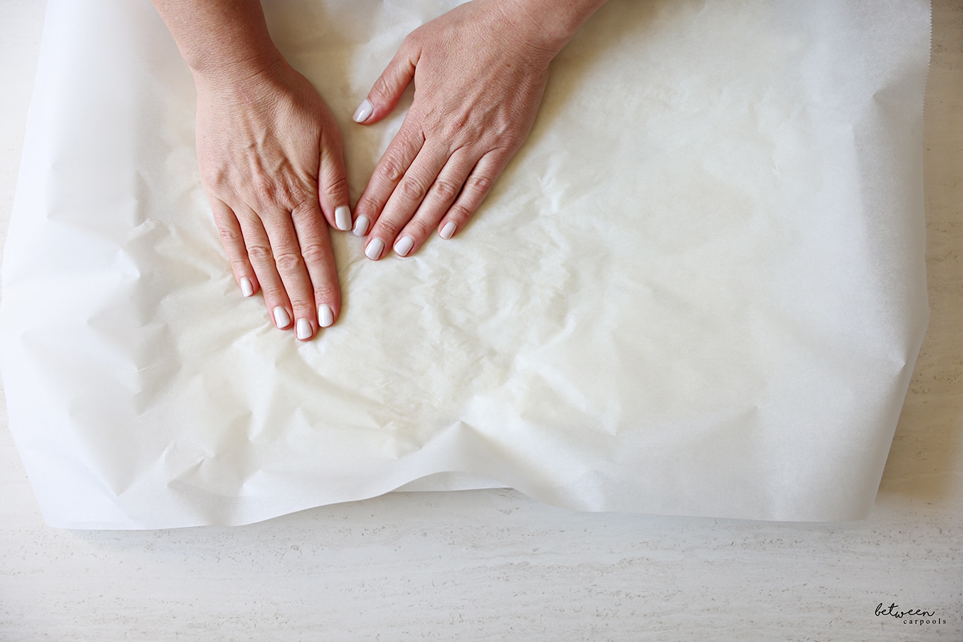Two hands on a sheet of parchment paper to smooth out sushi rice spread out on a parchment lined metal sheet pan. 