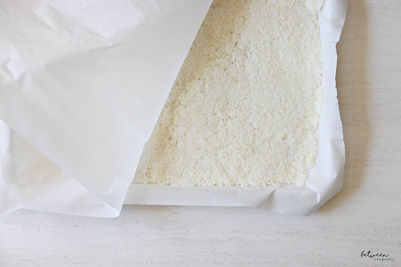 Tightly packed and an even layer of sushi rice on a parchment lined metal sheet pan.