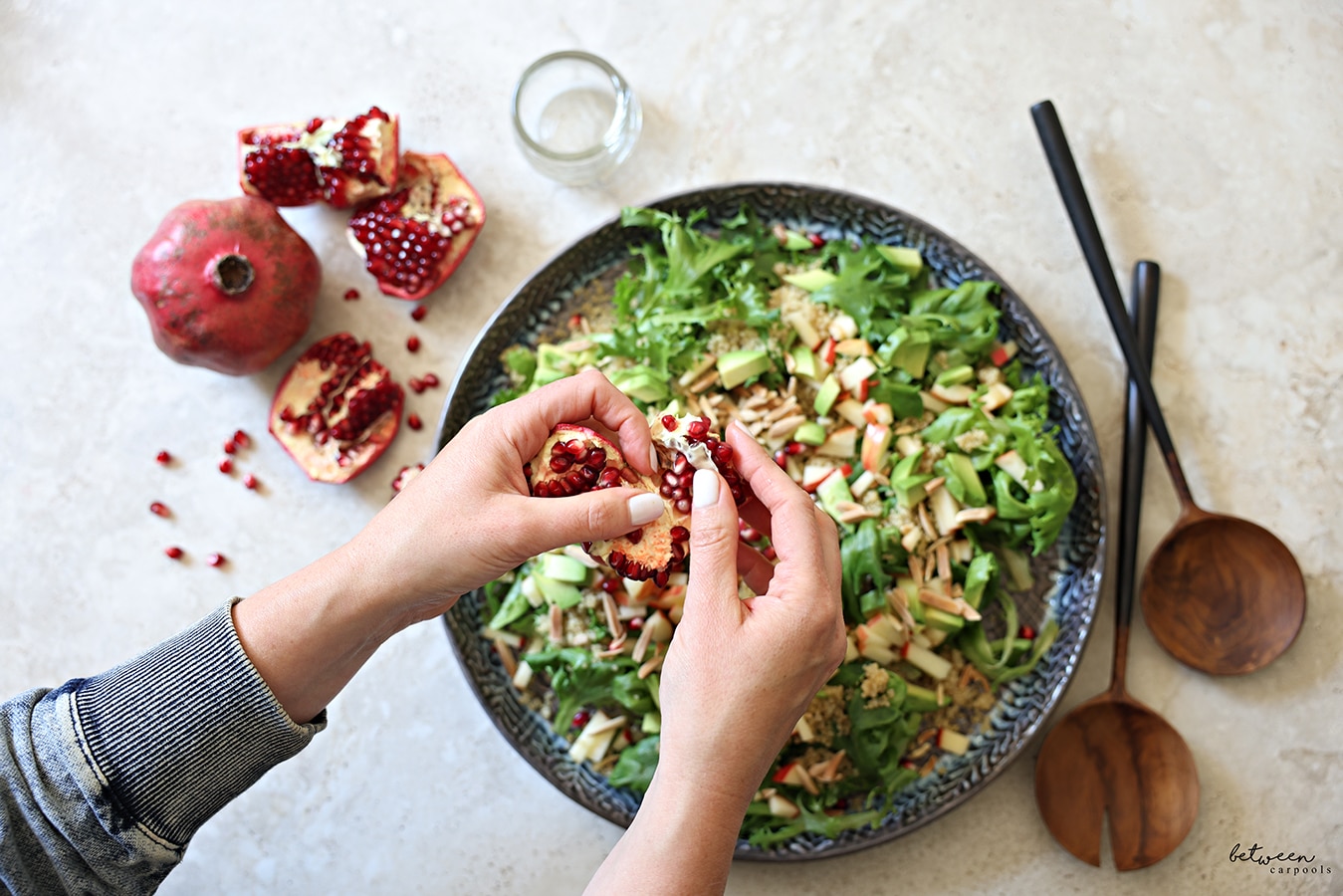 Seeding a pomegranate over plated greens with quinoa, avocado, and tiny cubed apple.