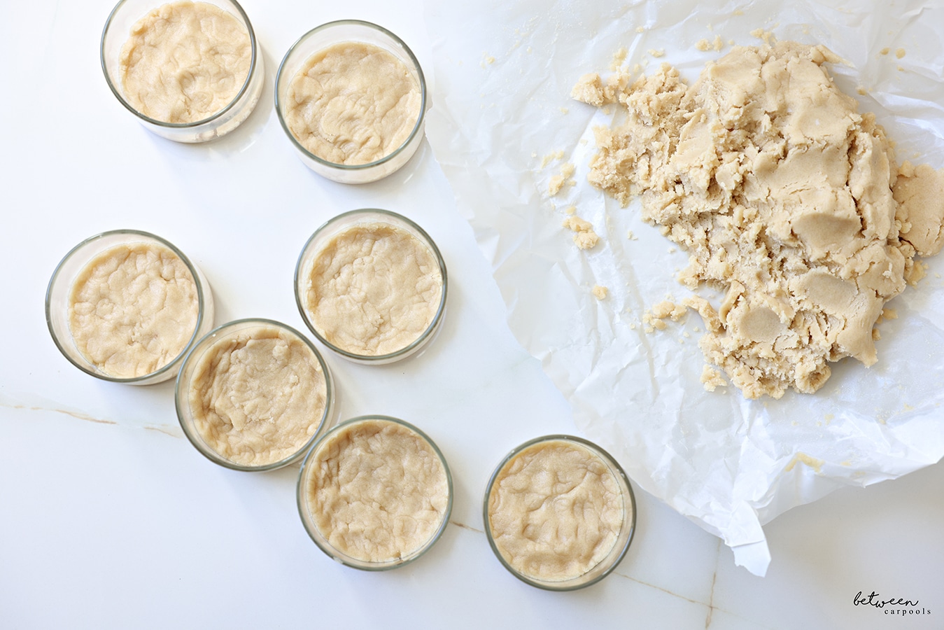 Top view of ramekins filled with shortbread cookie base. Crumbs nearby on parchment paper