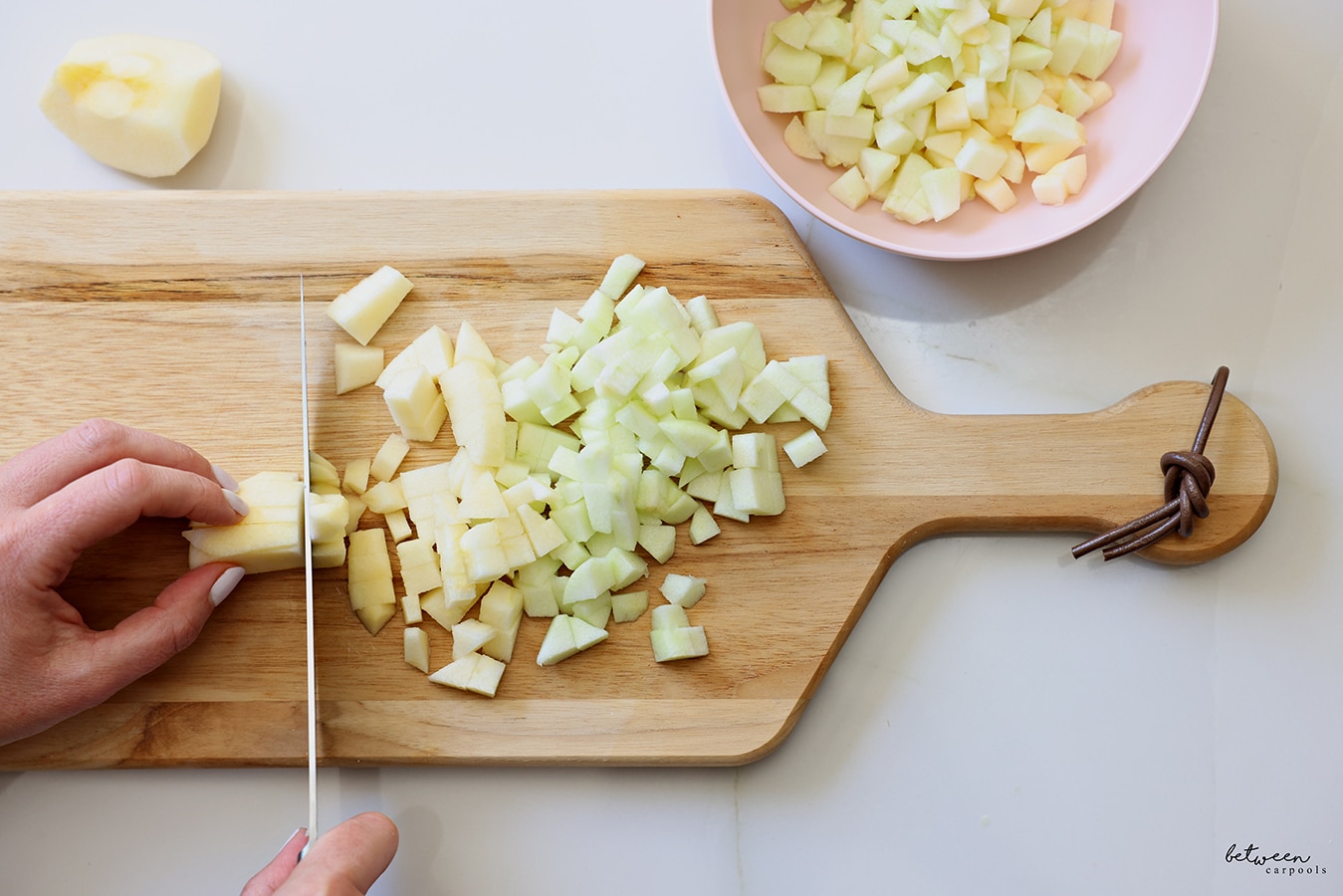 Dicing peeled apples on a cutting board. Diced apples in a bowl nearby