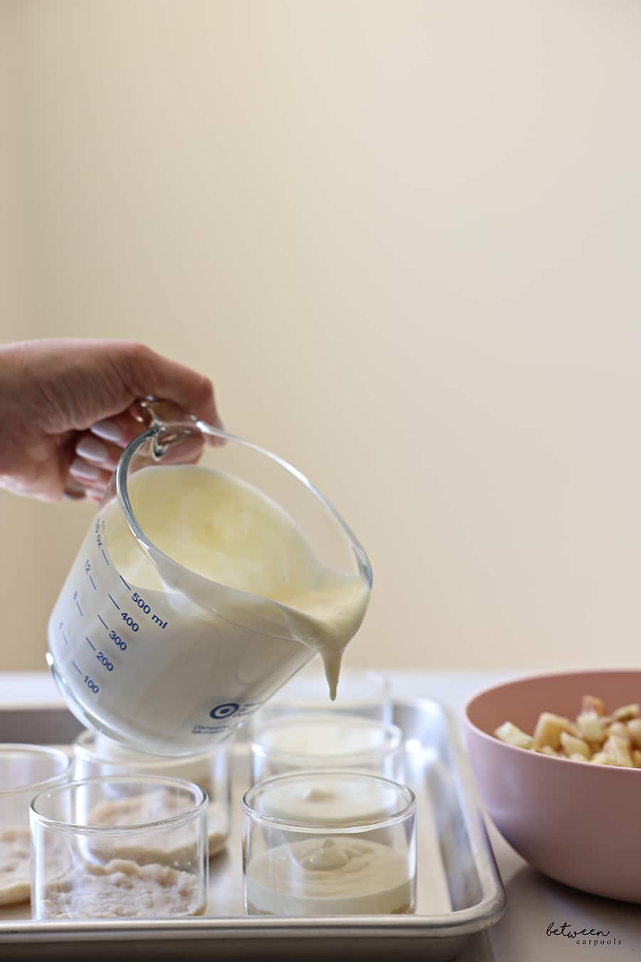 Pouring cheesecake mixture from a measuring cup into individual ramekins