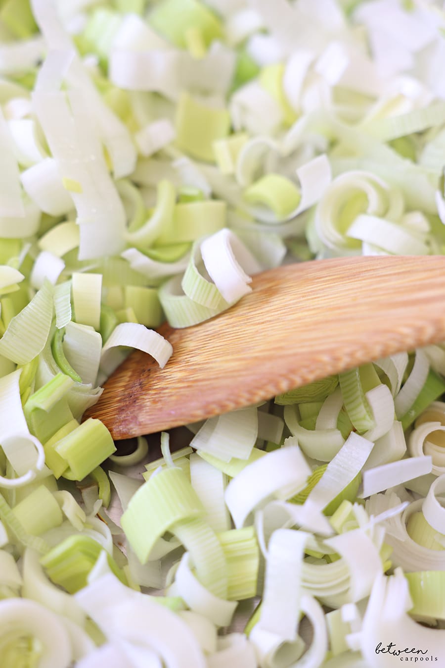 Leeks cut into half circles - in a pan with a wooden spoon