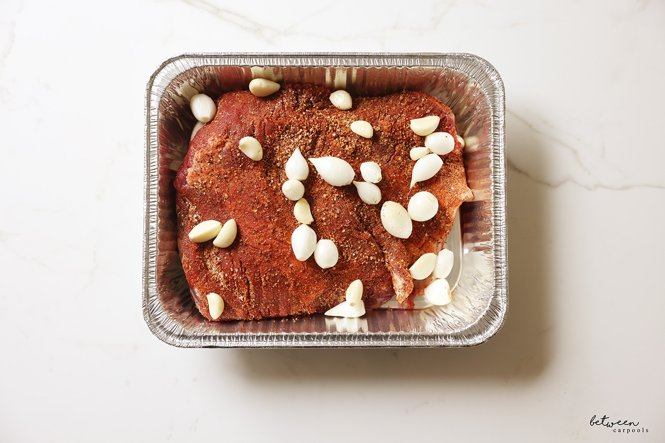 Brisket + pearl onions, garlic cloves, oil and seasoning in a baking pan ready for the oven