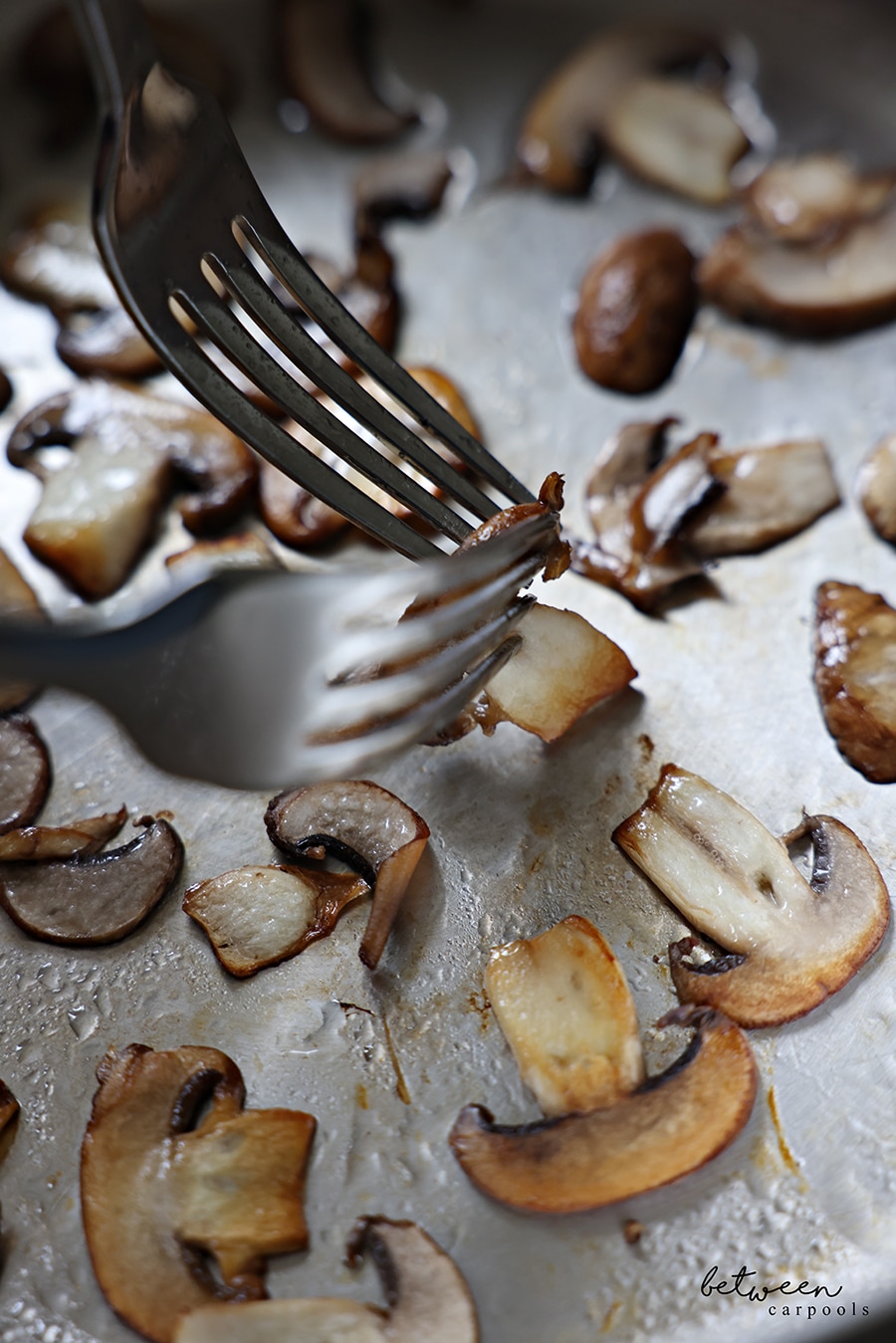 Removing sautéed mushrooms from pan with two forks.
