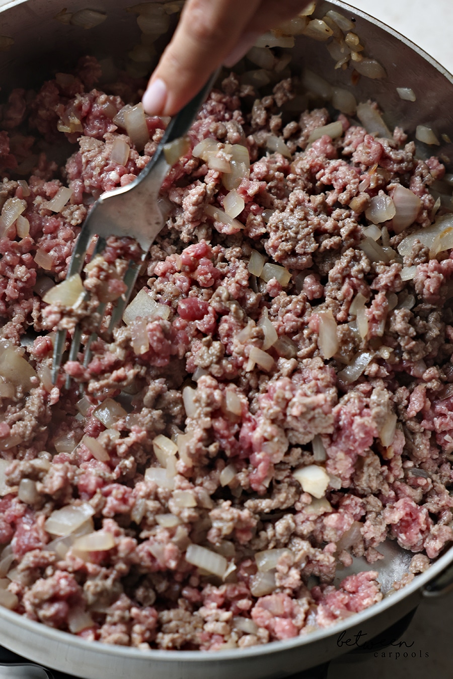 Breaking up ground beef in a sauté pan with a fork.