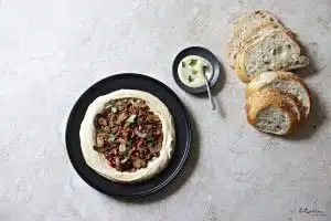 Plated chummus bassar with bread nearby.