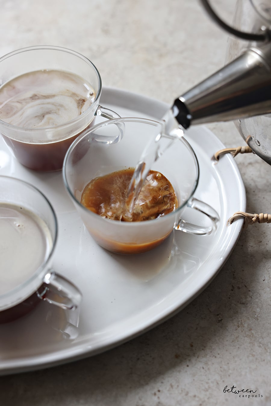 Pouring hot water into individual glass teacups with brown sugar and coffee.