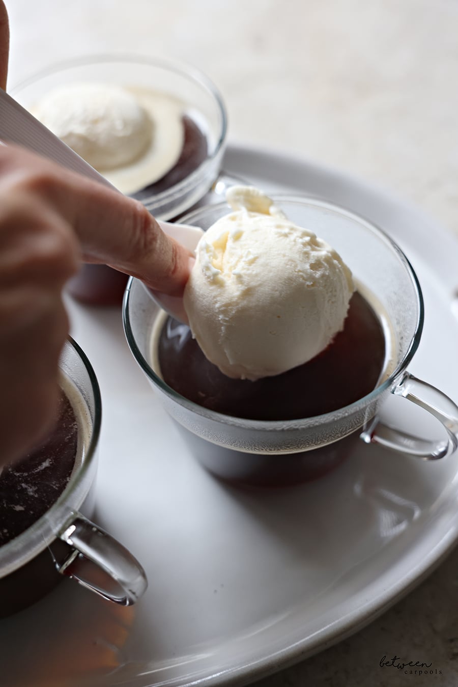 Adding a scoop of ice cream to each glass teacup with brown sugar, coffee, and hot water.