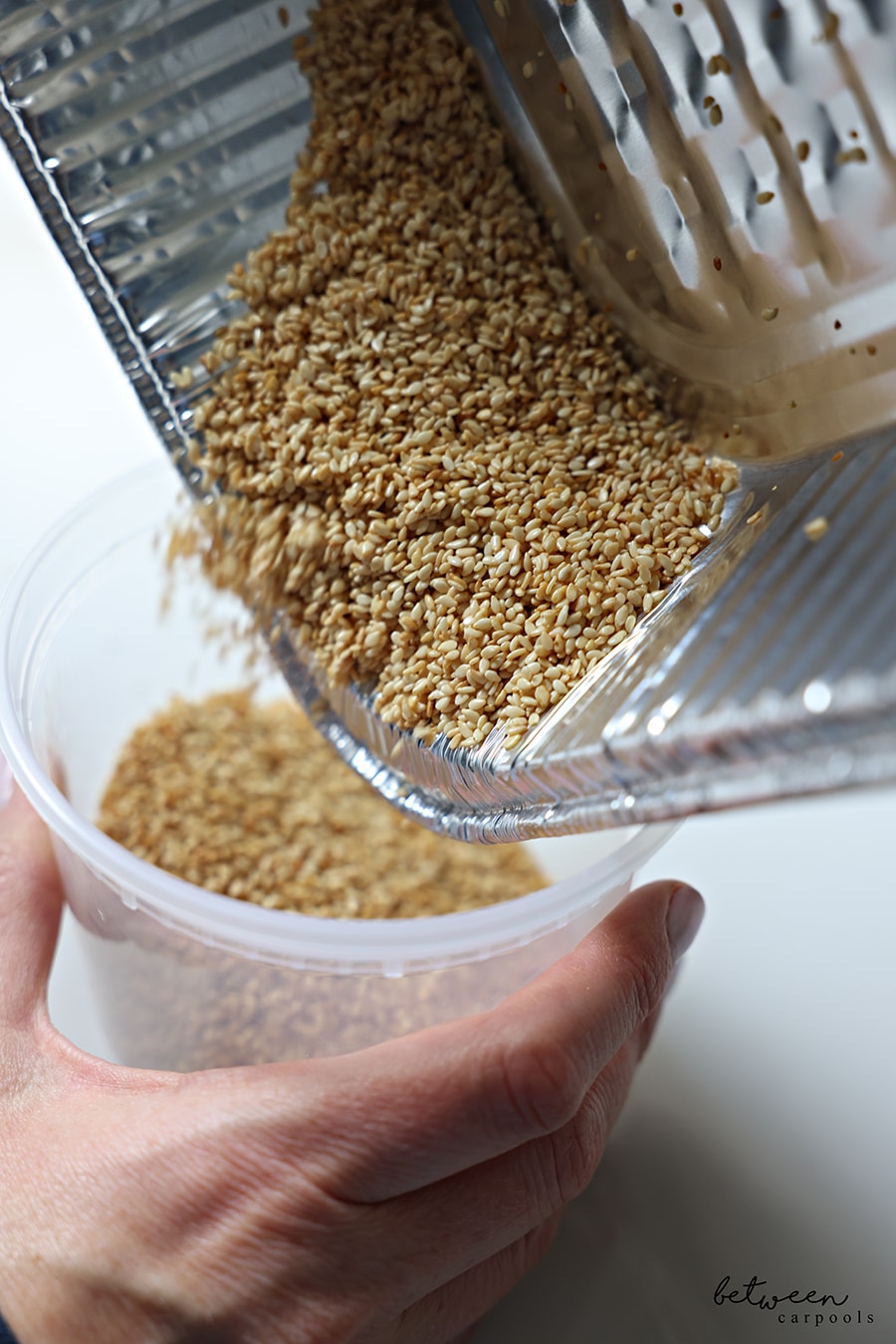 Pouring roasted sesame seeds into an airtight container.