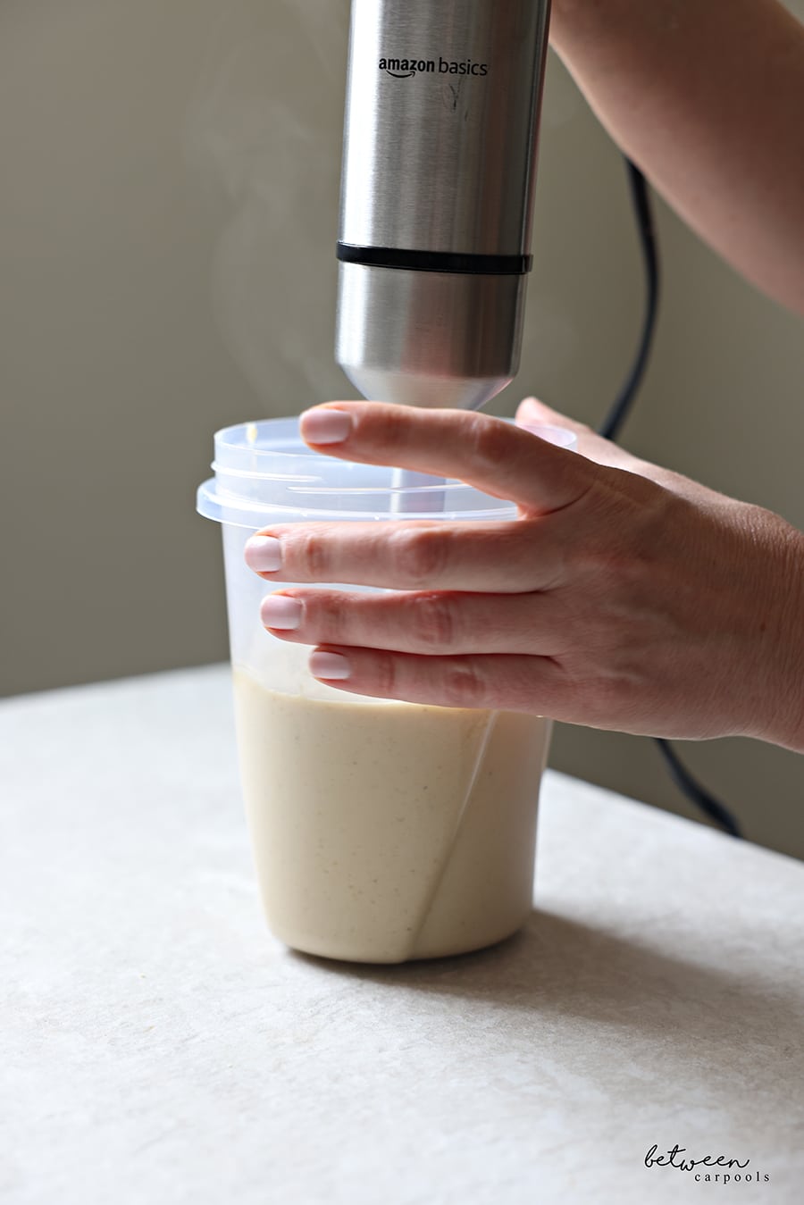 An immersion blender in a container with cream sauce.