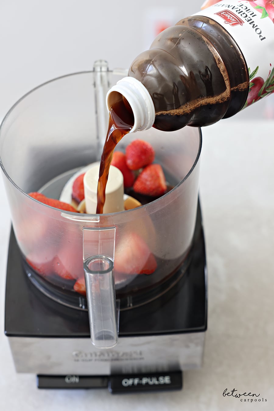 Pouring pom juice into food processor with frozen strawberries.