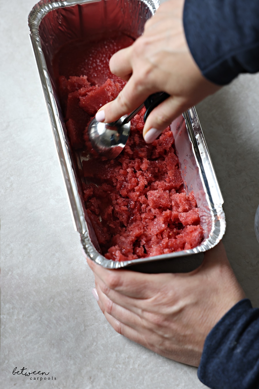 Scooping frozen strawberry pom mixture from a loaf foil pan.