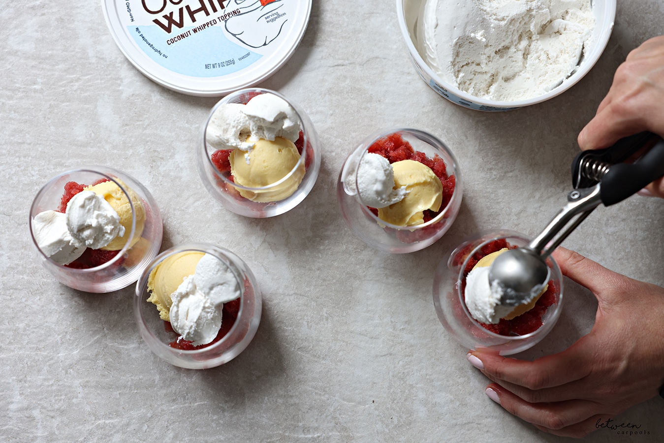 Adding Coco Whip to each glass cup with a scoop of pom- strawberry mixture and a scoop of sorbet.