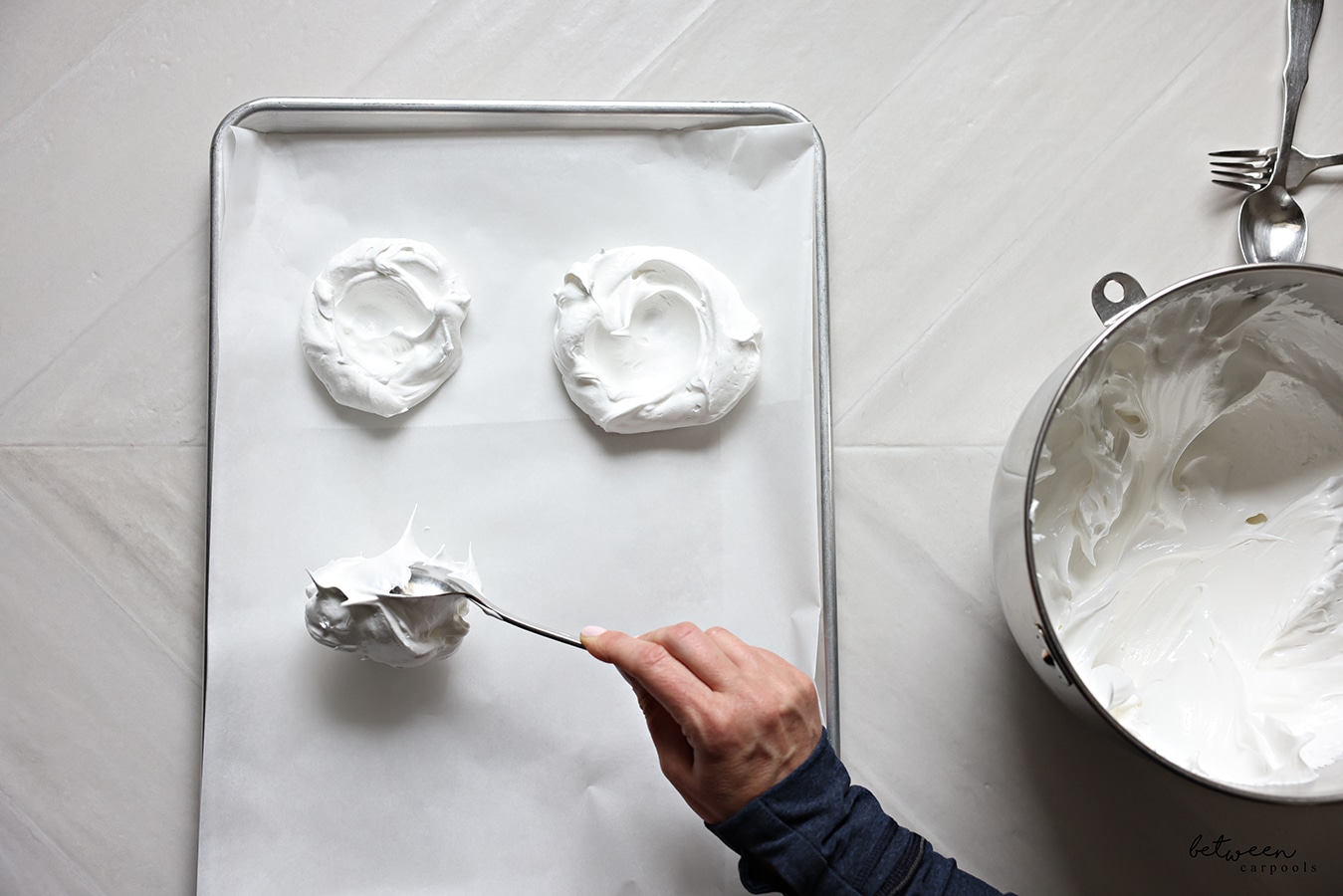 Placing a dollop of meringue on the sheet pan with a spoon.