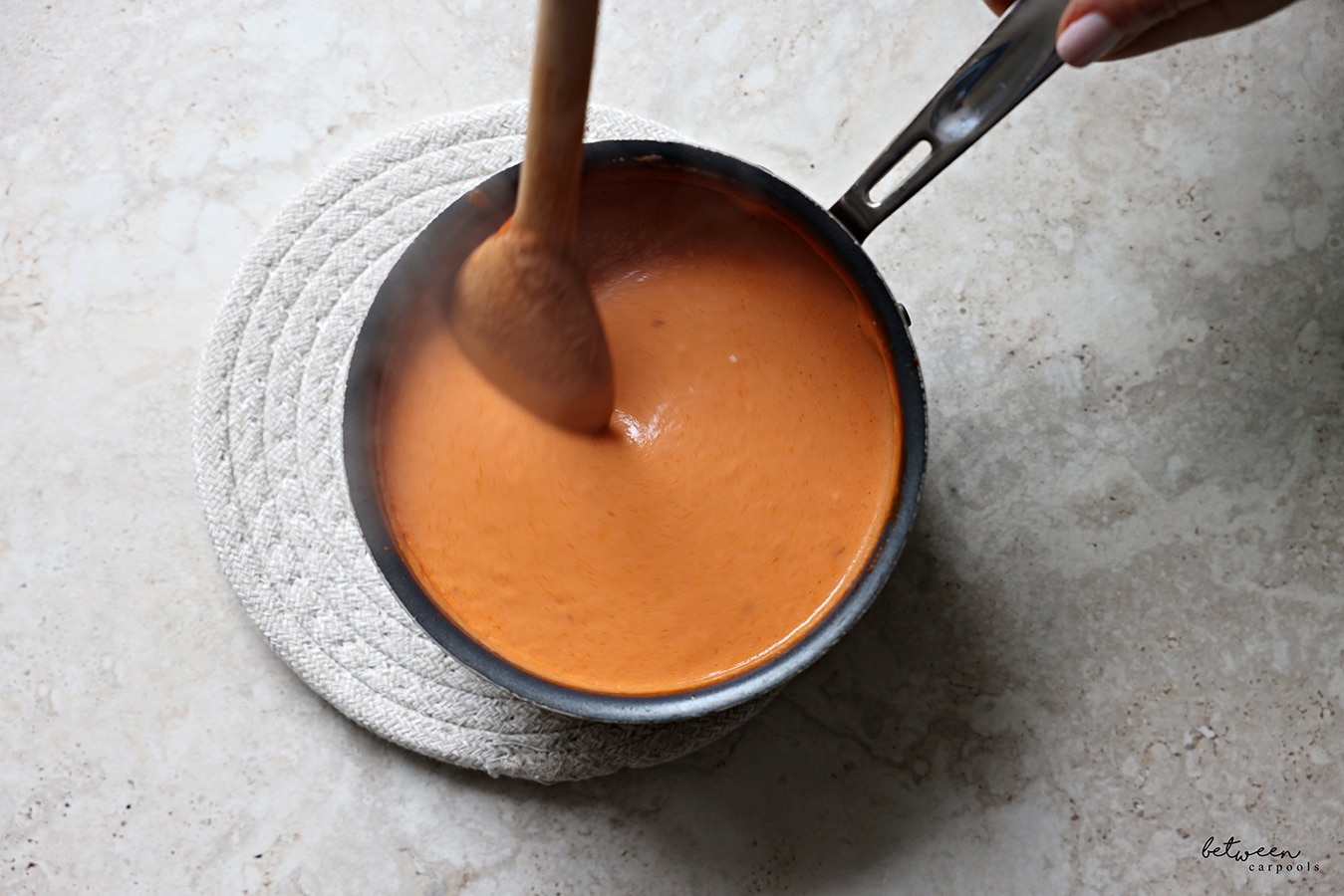 Mixing the tomato cream sauce in a pot with a wooden spoon.