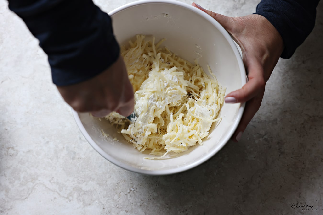 Mixing shredded cheese, salt and black pepper with cream cheese in a white bowl.