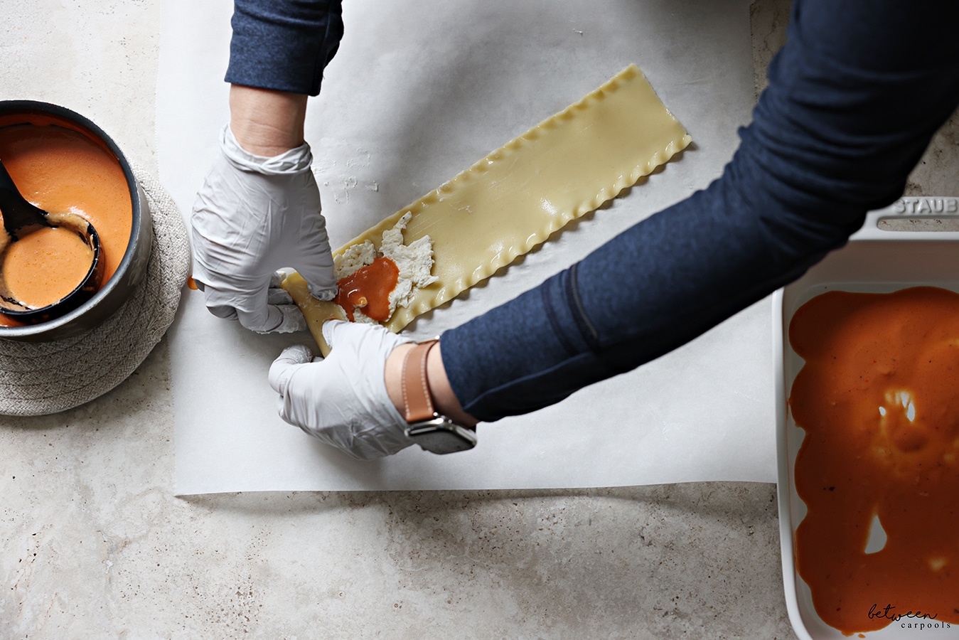 Starting to roll-up a strip of lasagna with cheese sauce and tomato cream sauce, on a piece of parchment paper.