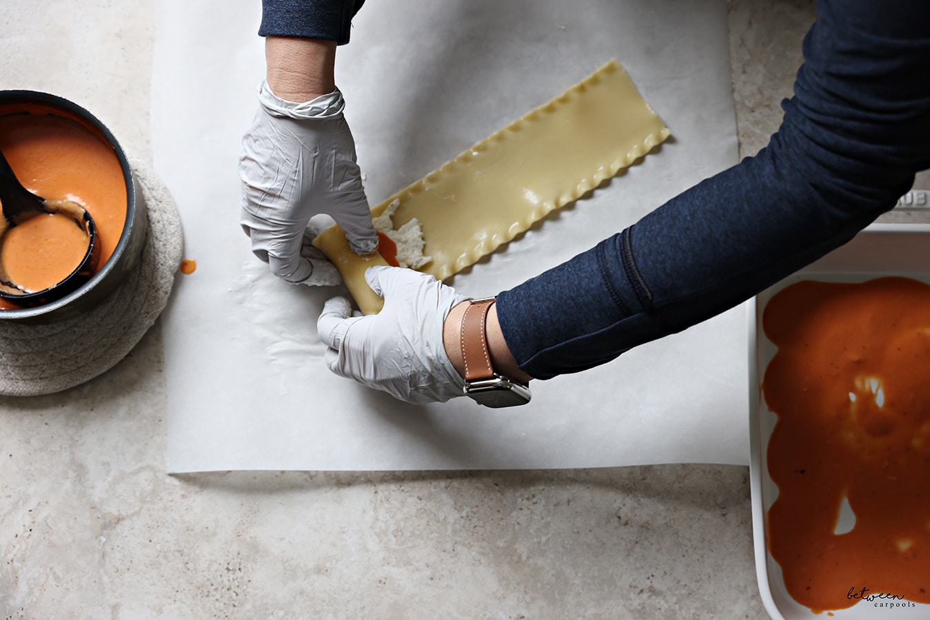 Rolling-up a strip of lasagna with cheese sauce and tomato cream sauce, on a piece of parchment paper.
