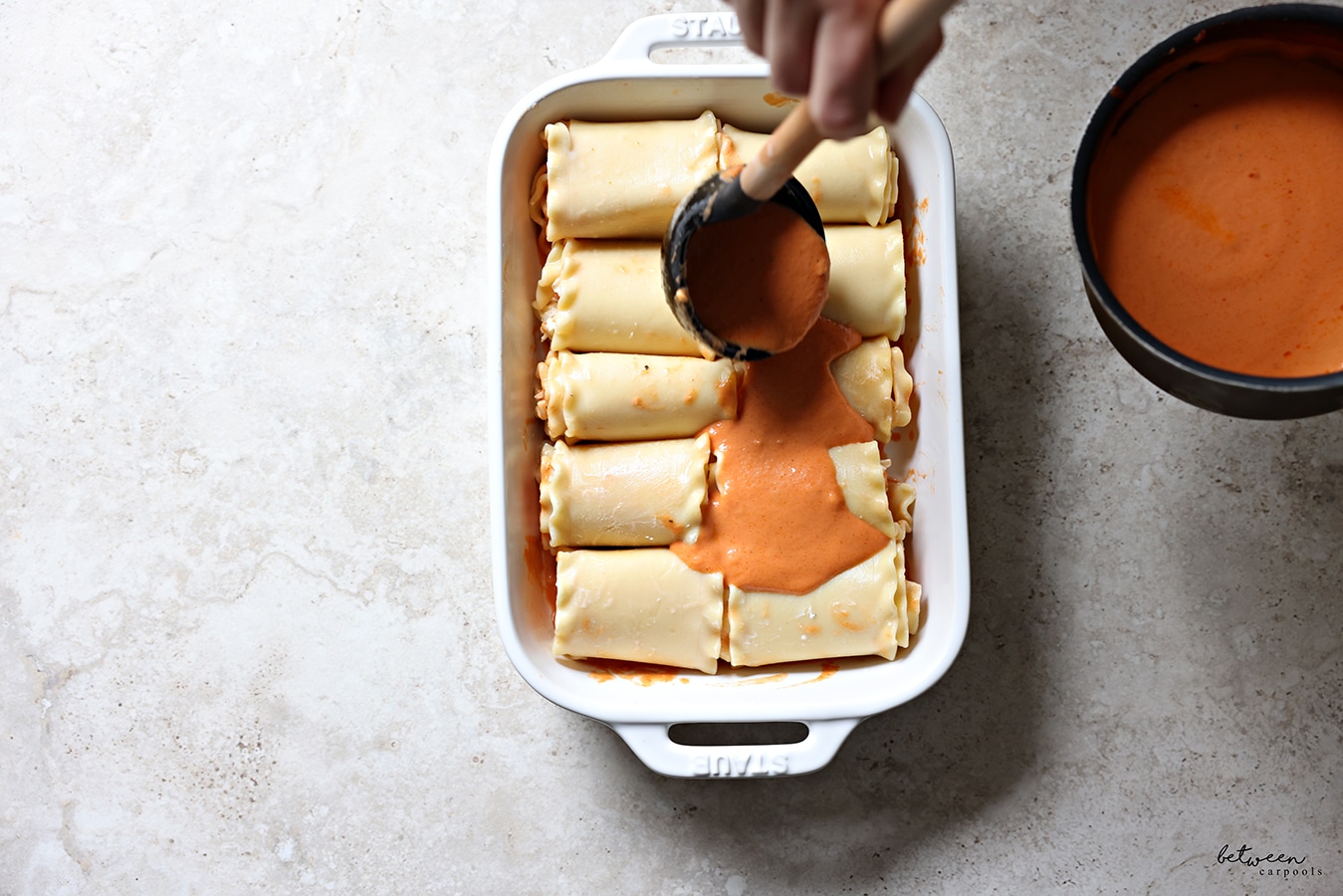 Topping all rolled lasagna sheets in a pan, seam side down, with remaining tomato cream sauce using a ladle.