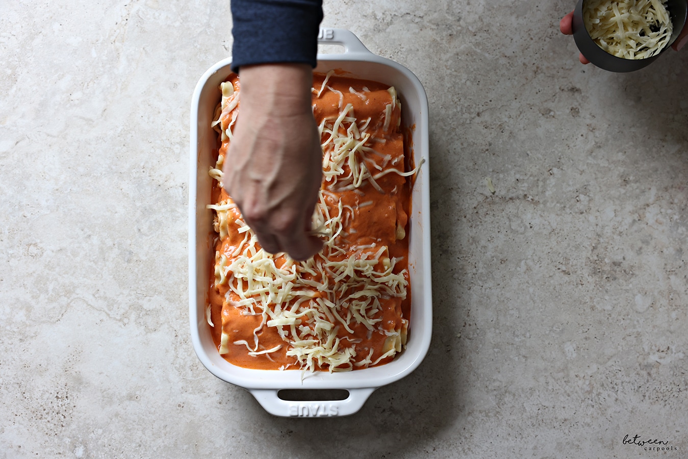 Adding cheese to all rolled lasagna sheets in a pan topped with tomato cream sauce.