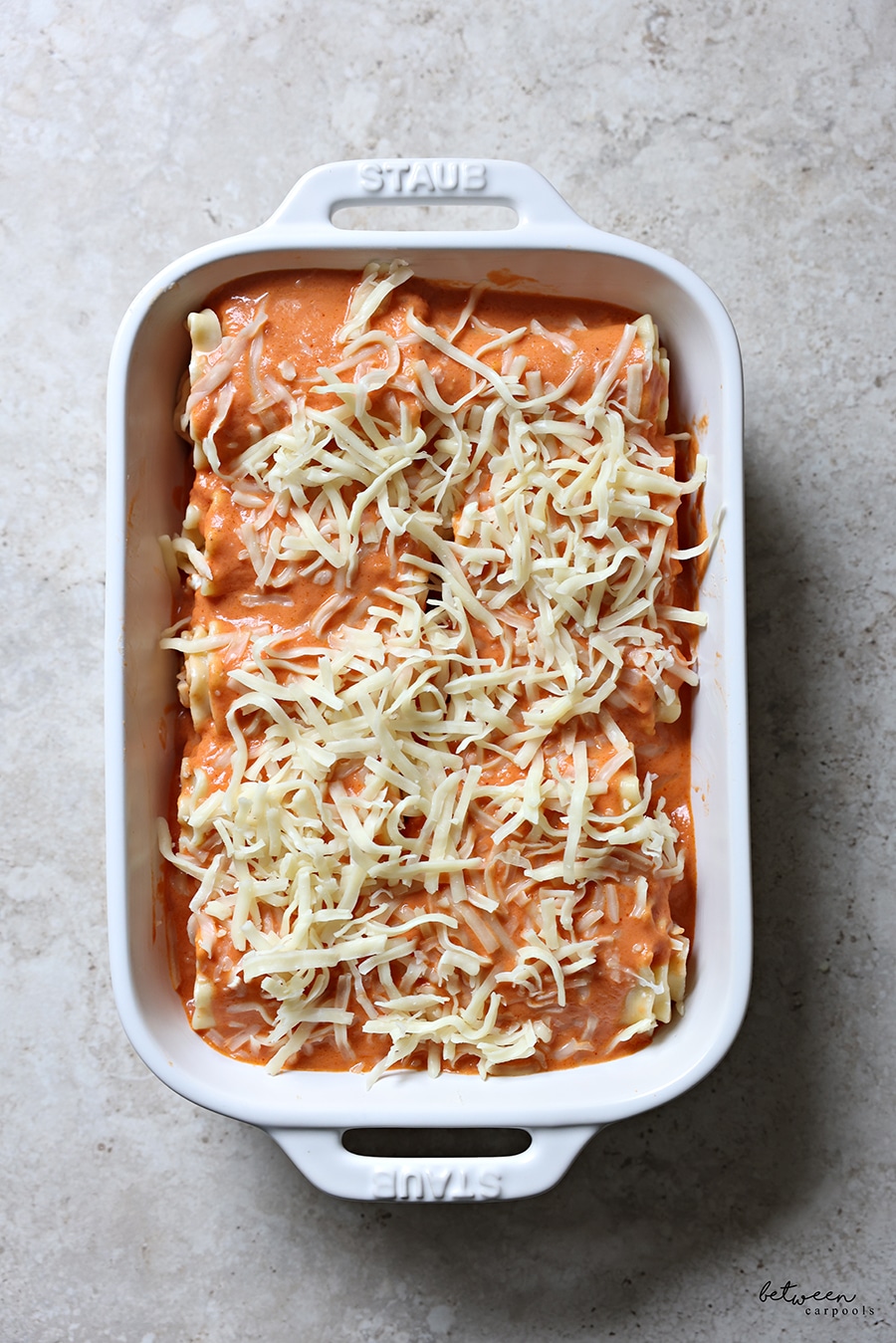 Rolled lasagna sheets in a pan topped with tomato cream sauce and cheese.