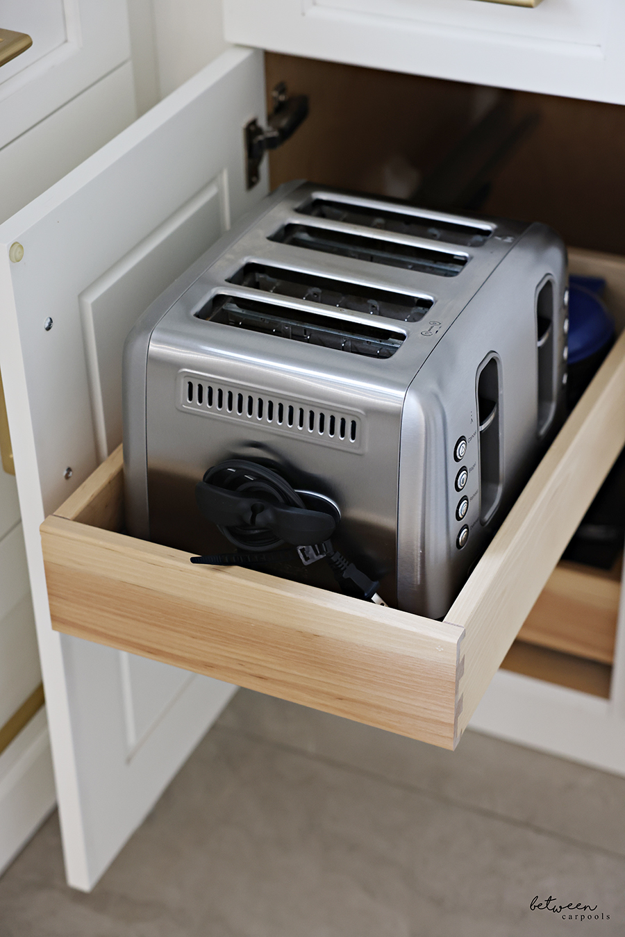 Toaster with its wire wrapped around an appliance cord wrap on a pull out shelf in a kitchen cabinet.