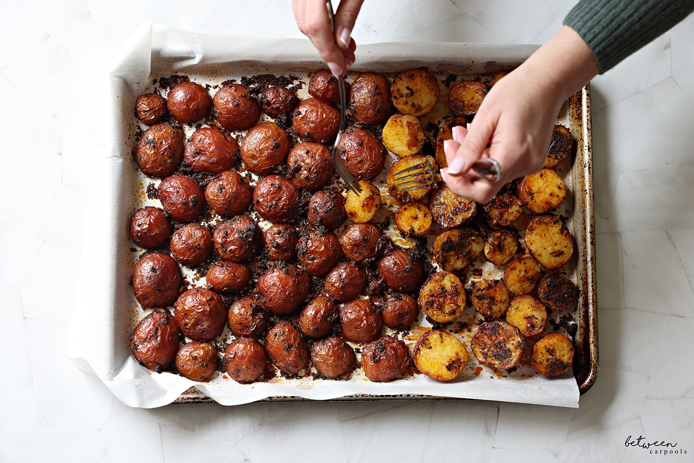 Flipping baked red potatoes on a parchment lined baking sheet.