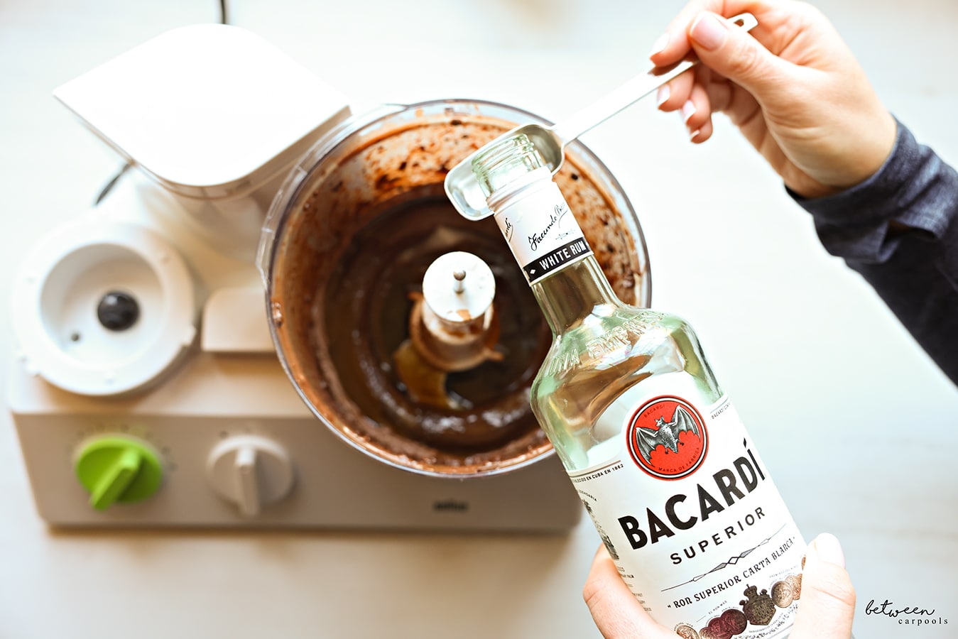 Adding Bacardi rum to puréed chocolate with coffee and sugar in the bowl of a food processor fitted with the “S” blade.