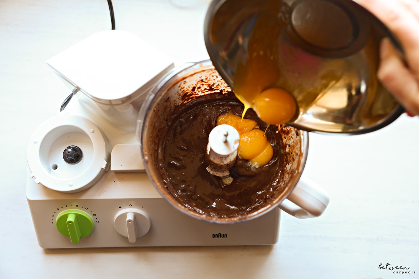 Adding egg yolks to puréed chocolate with coffee, sugar and rum, in the bowl of a food processor fitted with the “S” blade.