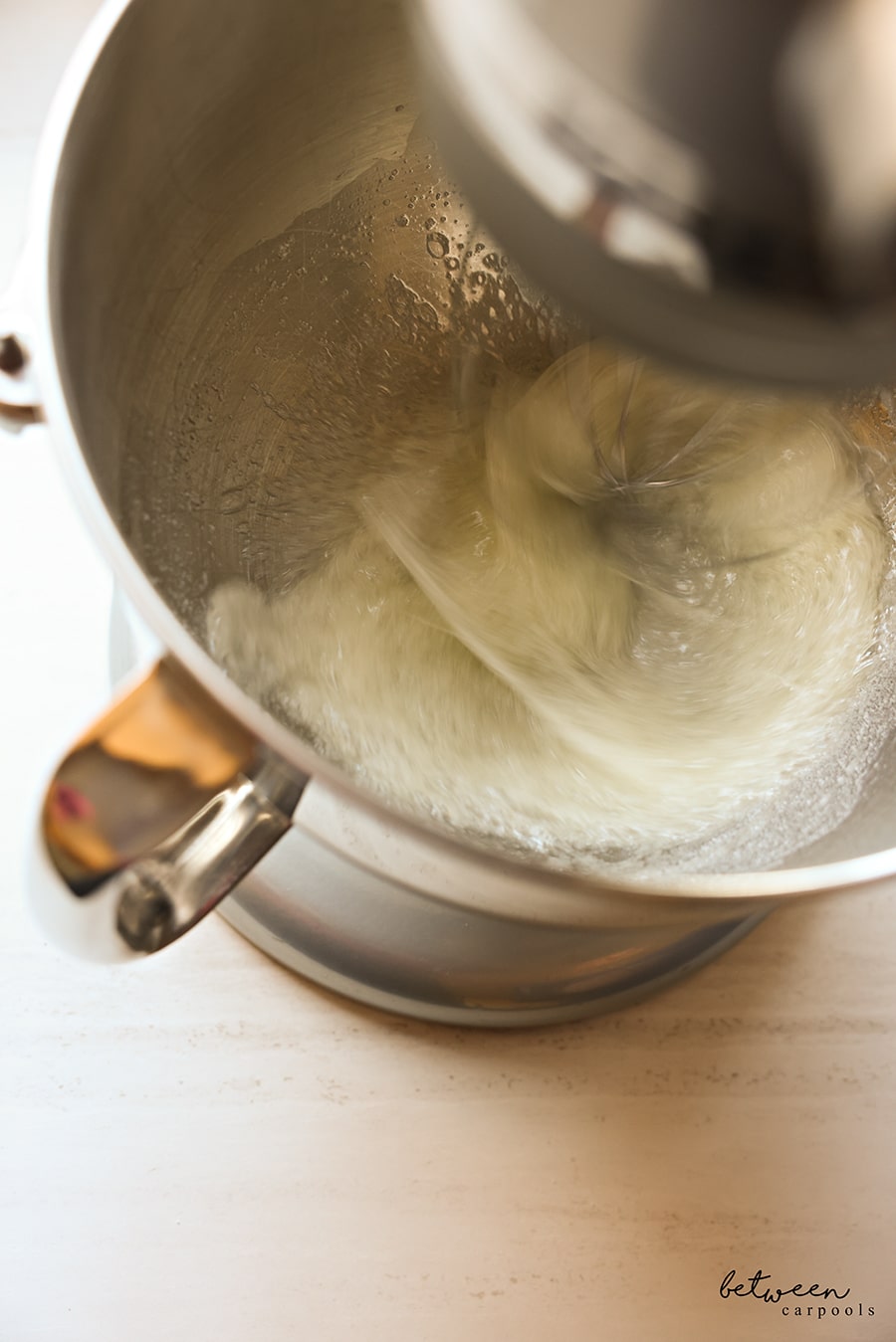 Beating egg whites in a Kitchen Aid mixer until stiff peaks form.