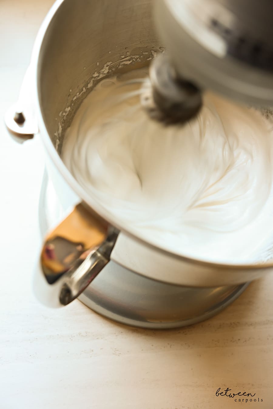Stiff egg white peaks in the bowl of a Kitchen Aid mixer.