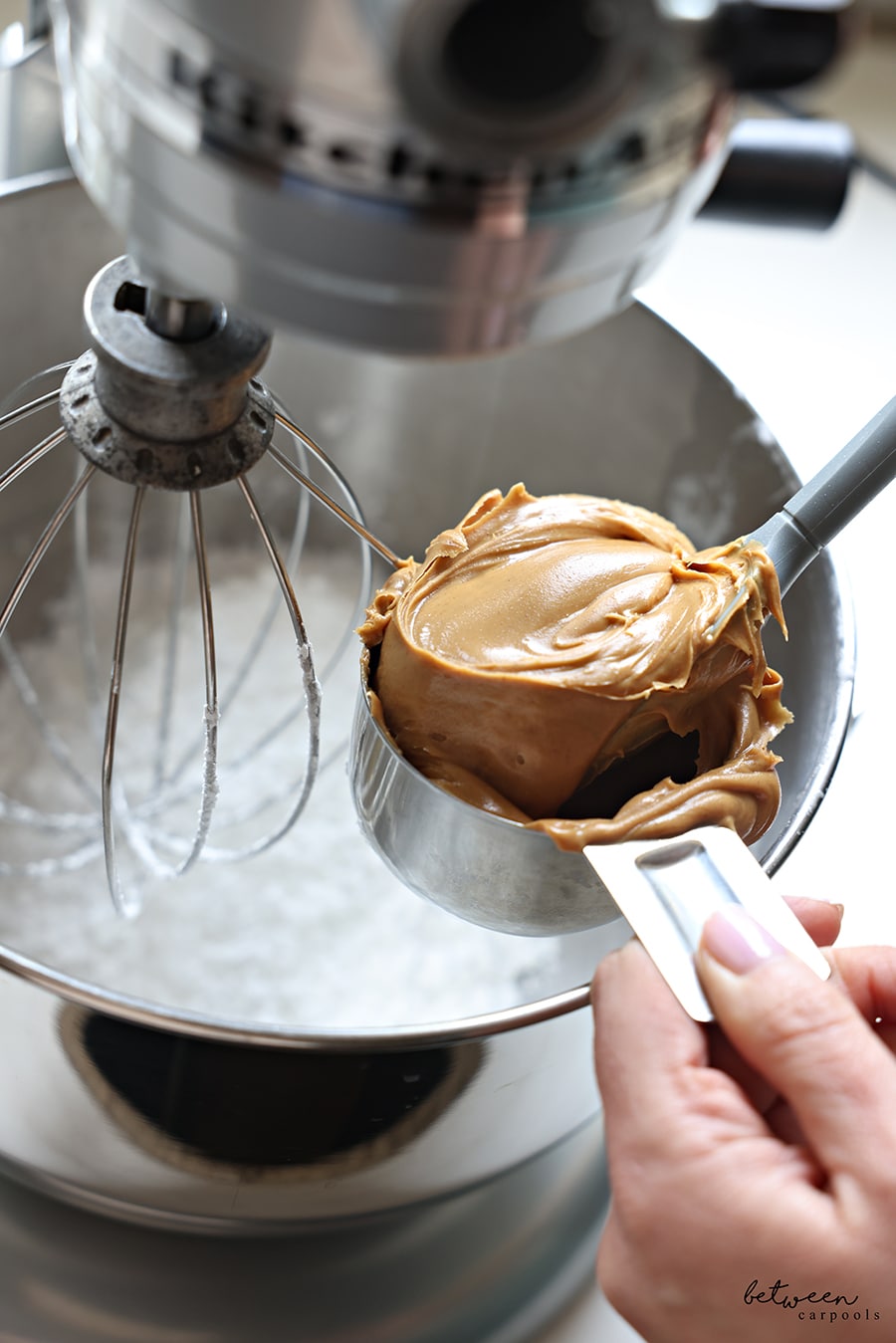 Adding peanut butter to the bowl of a Kitchen Aid mixer with confectioner's sugar.