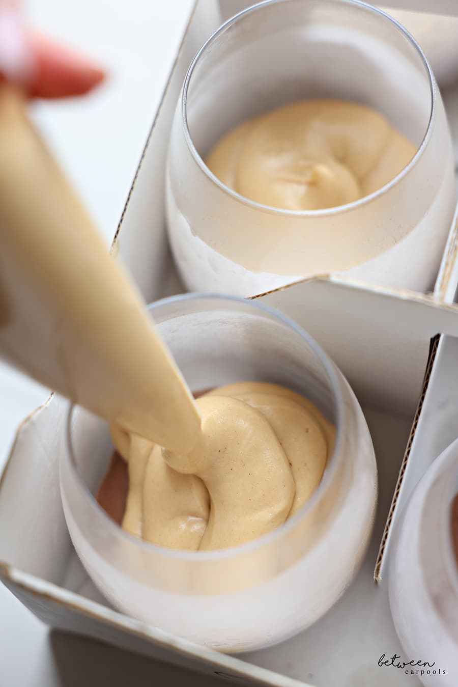 Piping peanut butter mousse over the chocolate layer in glass cups.