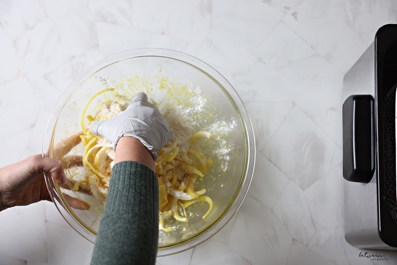 Tossing onion strings tossed with honey, mustard, and vinegar with flour, salt, and chili powder in a pyrex bowl.