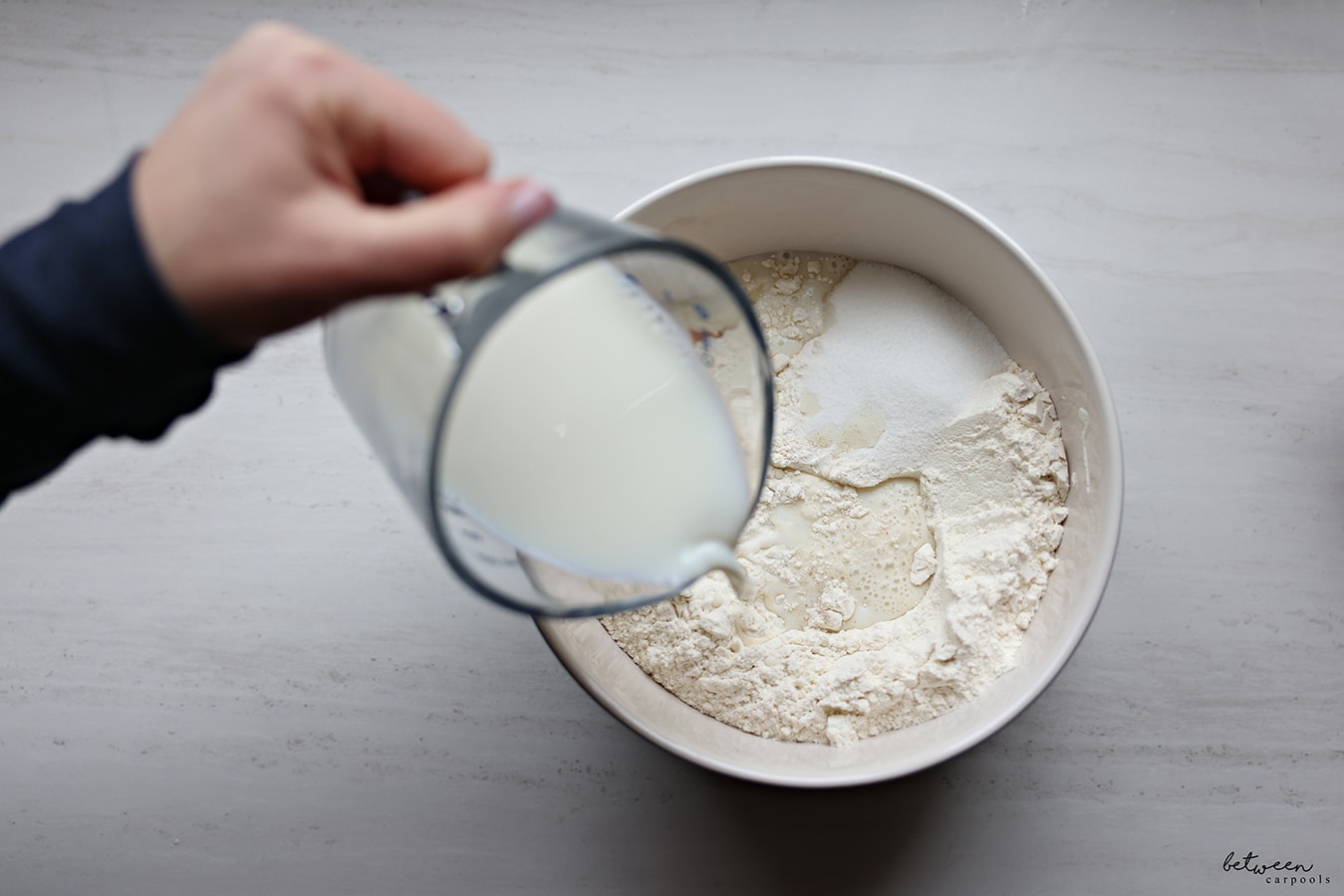Adding milk to a bowl with flour, sugar, eggs, and dry yeast.
