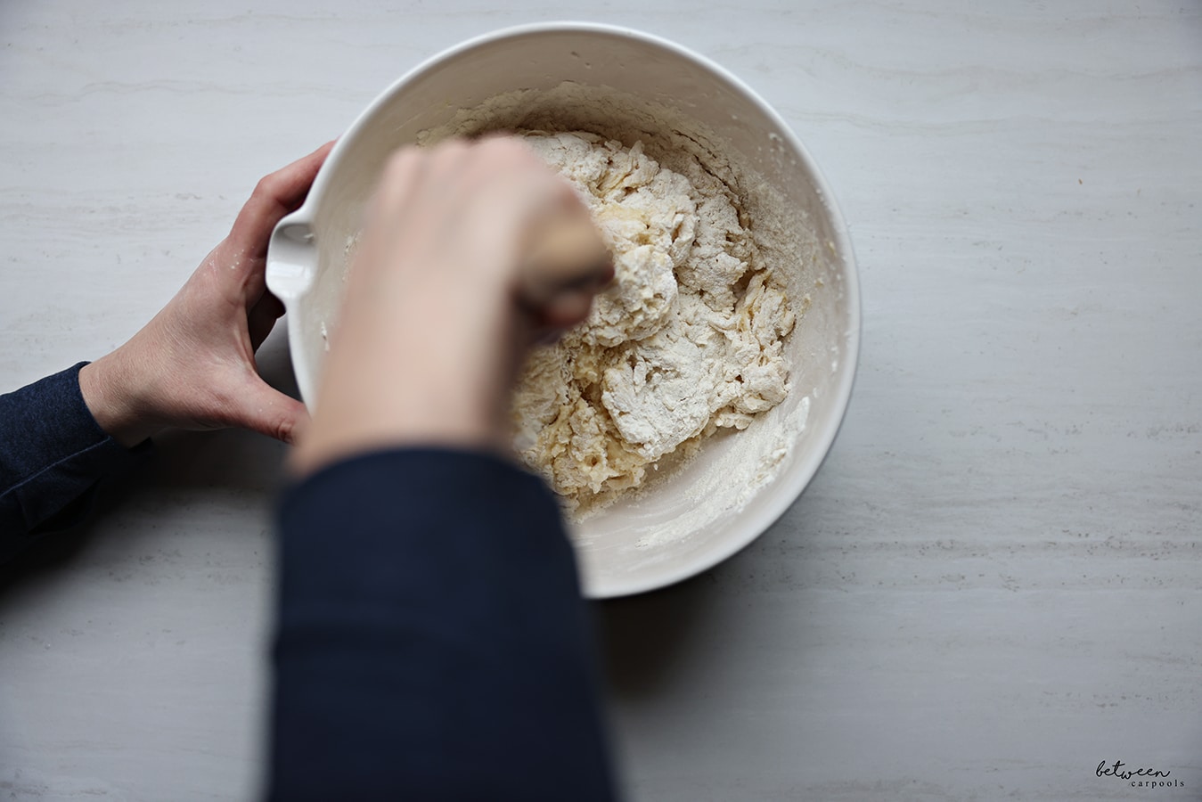 Mixing the flour, sugar, eggs, yeast and milk with a wooden spoon.