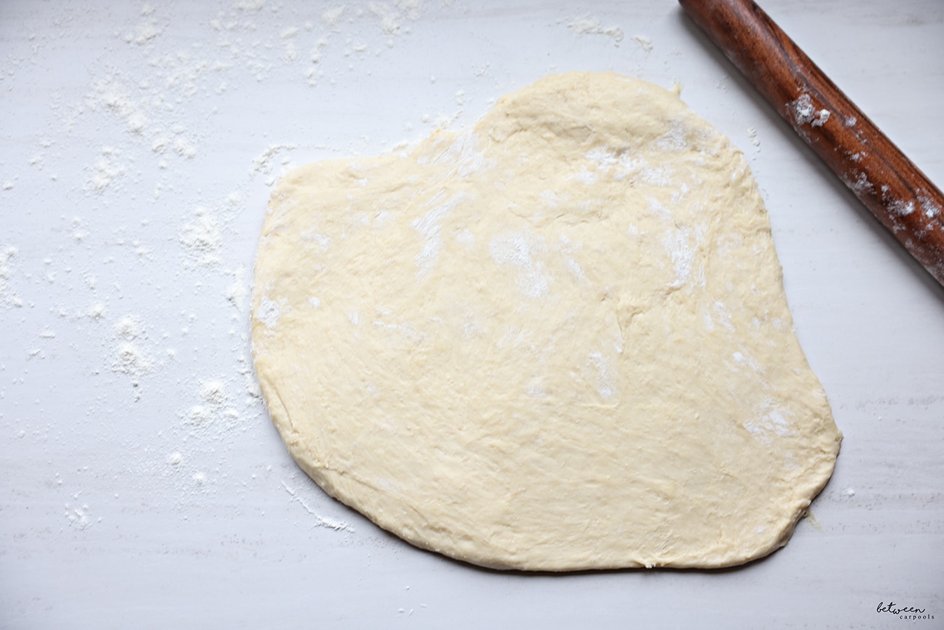 Dough rolled to a half-inch-thick rectangle on a floured counter. Wooden rolling pin.