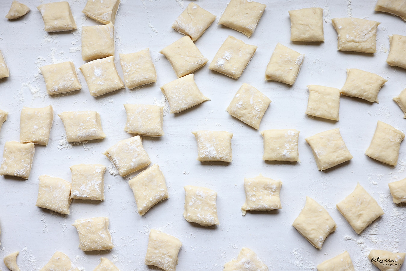 Lots of squares of rolled dough on a floured counter.