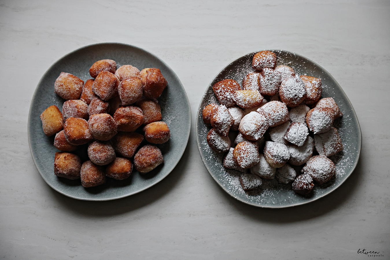 One plate of beignets tossed in sugar and a plate of beignets sprinkled with confectioner's sugar.