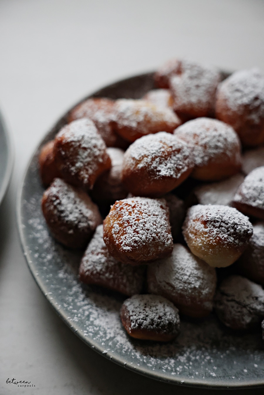 Closeup of a plate of beignets sprinkled with confectioner's sugar.