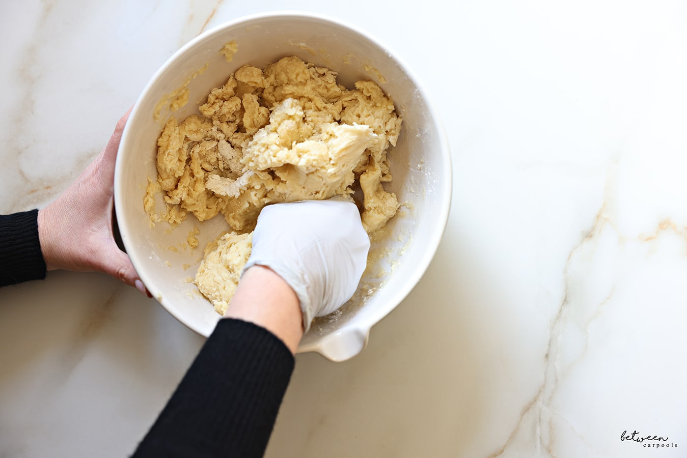 Kneading flour, baking powder, oil, and orange juice in a bowl with a gloved hand.