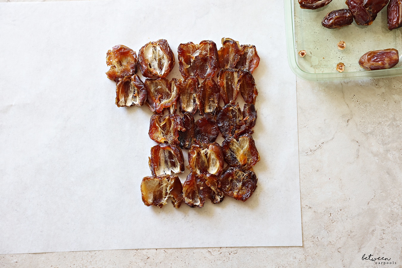 Pitted dates, laying open down, on parchment paper.