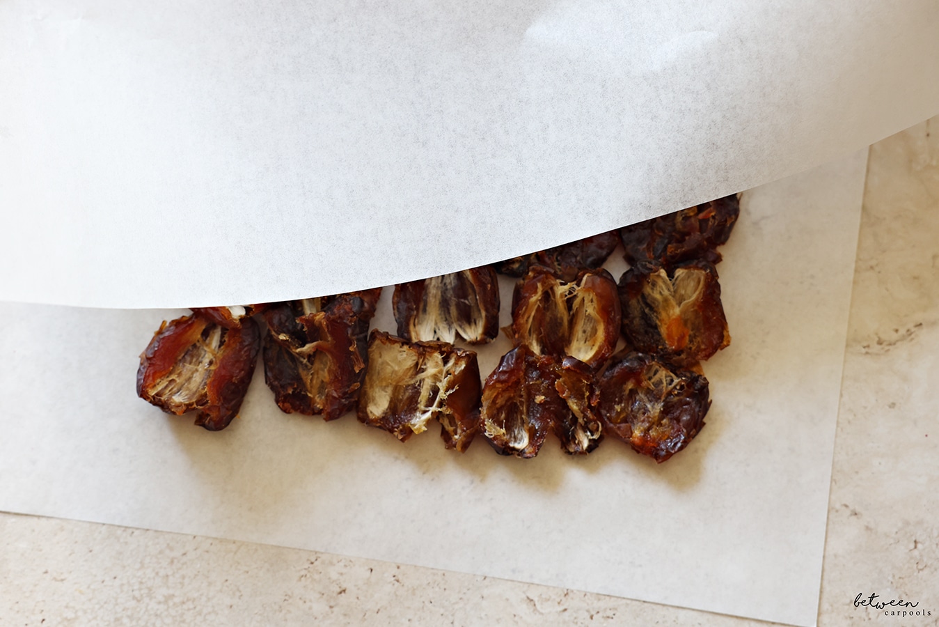 Placing another piece of parchment over pitted dates, laying open down, on parchment paper.