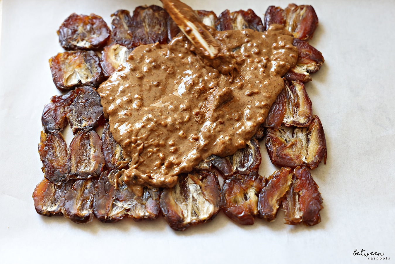 Spreading a layer of nut butter over the flattened layer of dates on parchment paper.