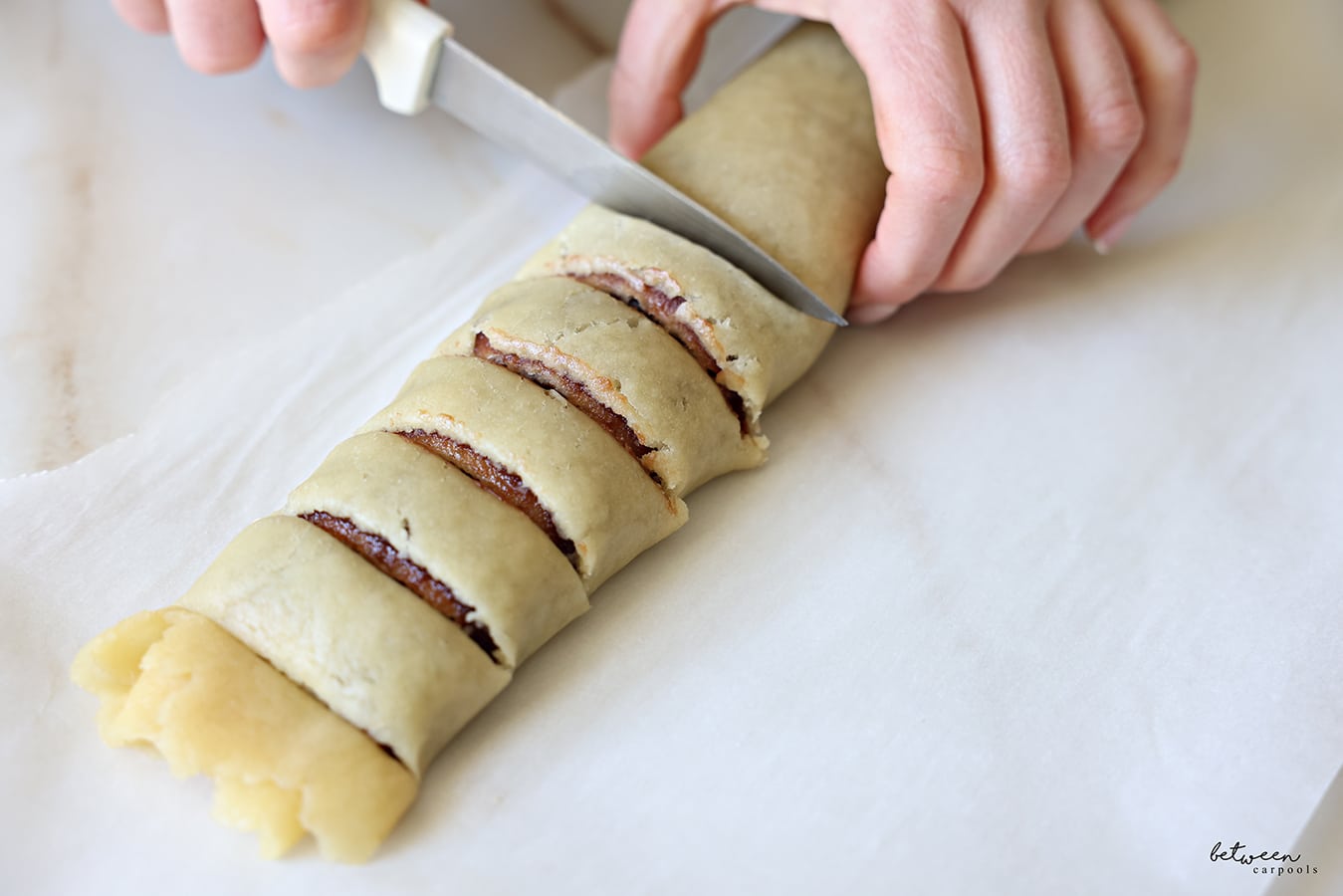 Cutting slits in date filled rolled dough jelly-roll style on a parchment lined baking sheet.
